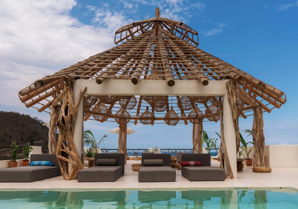A wooden cabana at Xeno Hotel equipped with cane lamps, comfortable loungers overlooking the pool.