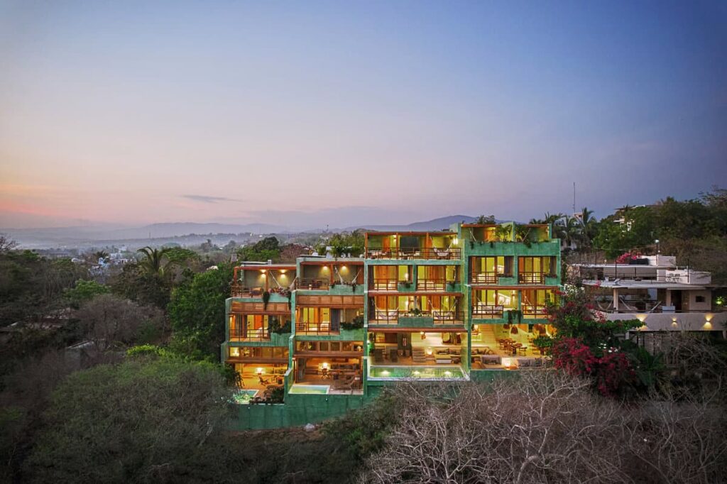 A view of Punta Nayaa boutique hotel from a distance showcasing rooms with balconies and outdoor pool and surrounded by lush greenery.