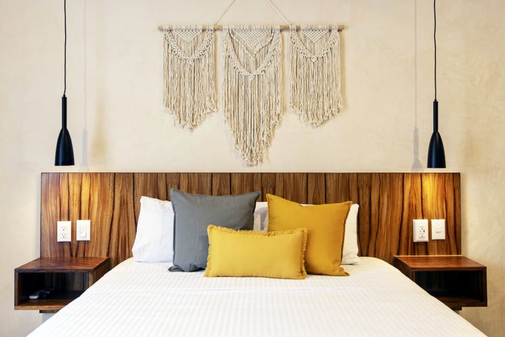 A view of bedroom at Casa Ita Surf with a large macrame wall hanging over the wooden headboard and bright colored pillows.