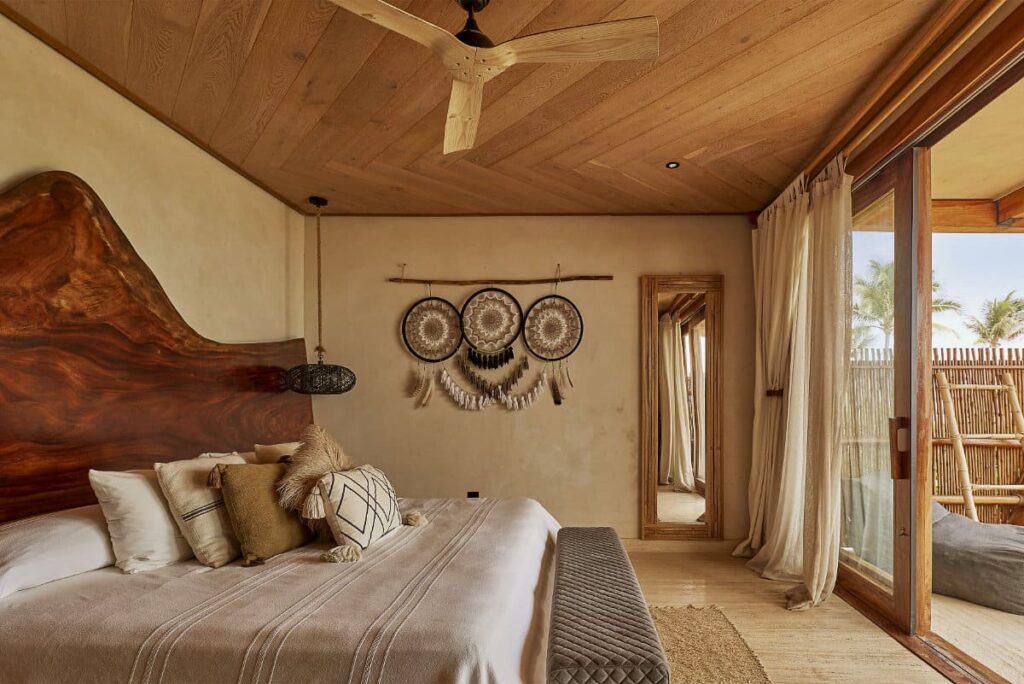 A view of a bedroom at Casa Joseph furnished with a large wooden headboard, quality furnishings, dreamcatchers, a tall mirror and wooden doors leading to a private outdoor space.