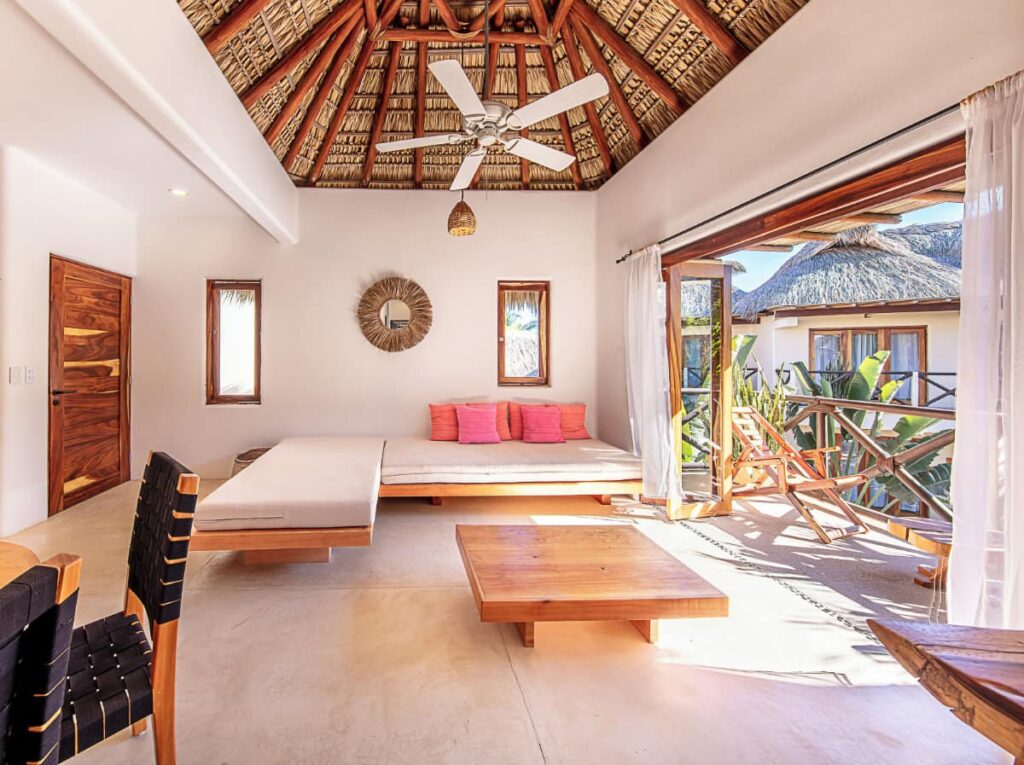 The bright and airy bedroom at Casa Kuaa with a thatched ceiling, a ceiling fan, wooden accents and a private outdoor space.