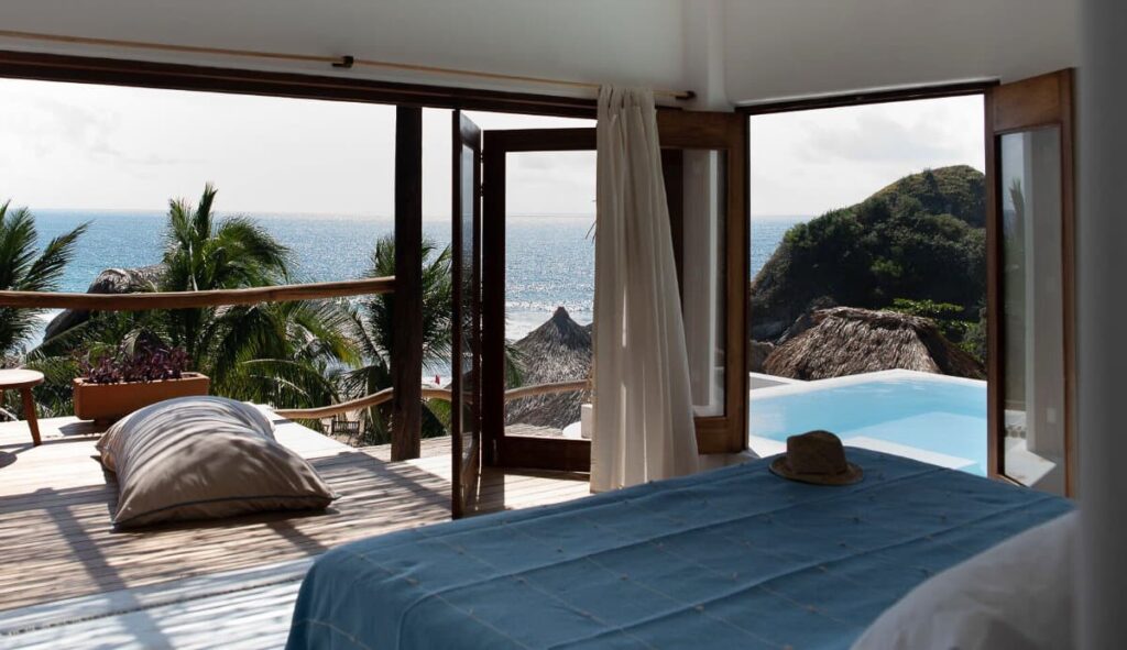 A room at El Alquimista that come with a balcony and outdoor pool surrounded by palm trees, lush green hills and an ocean view.