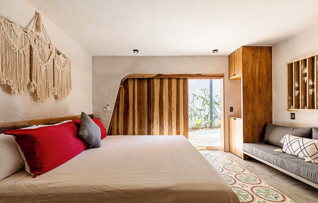 A bright and airy room at Quiote Quiote boutique hotel furnished with a large macrame wall hanging, a spacious bed and seating space and wooden cabinet and sliding door.