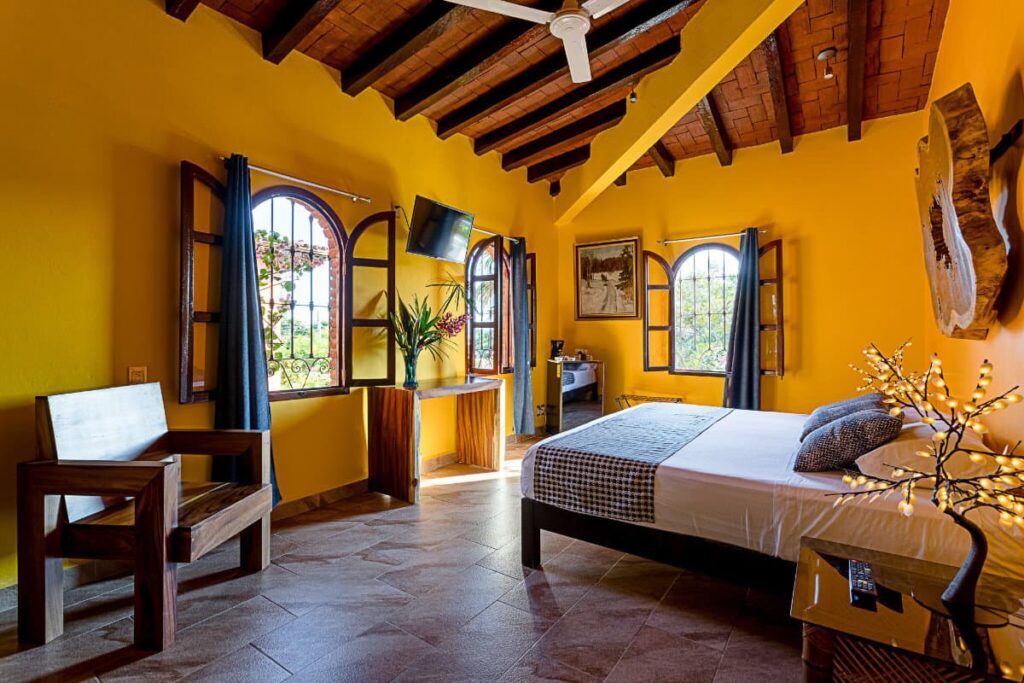 A yellow-colored room at Suites La Hacienda furnished with wooden furniture, a ceiling and windows.