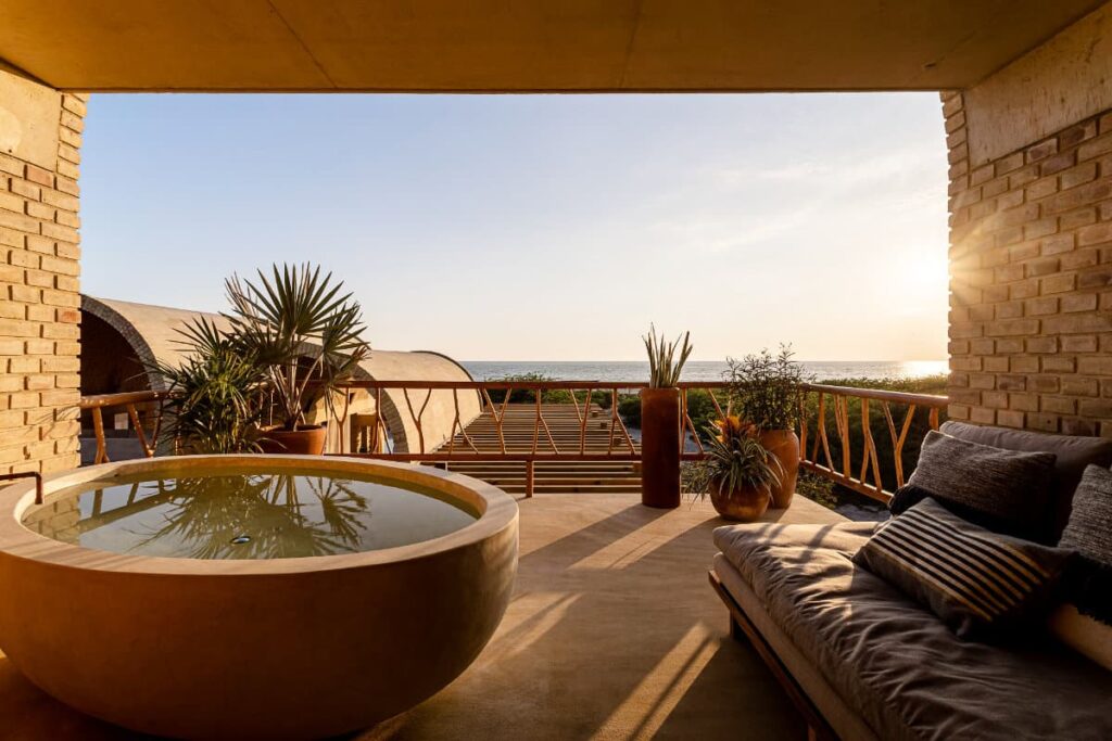 A view of a tub in the balcony area of Casa Sforza along with additional seating space, potted plants and a view of ocean and setting sun.