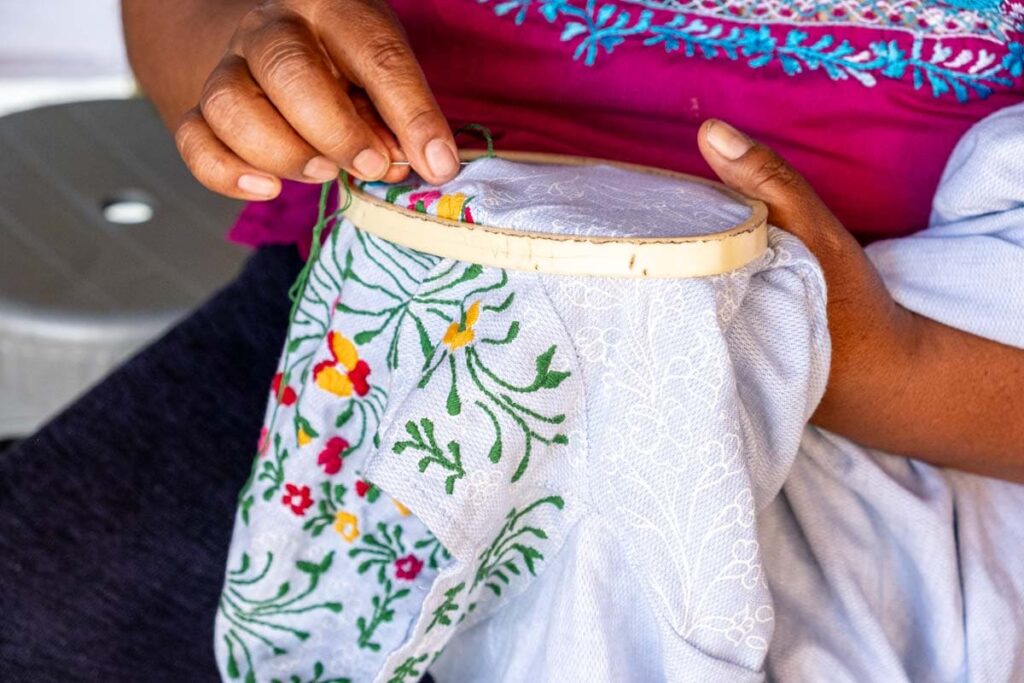 A close up of a woman embroidering a white piece of fabric with green vines and bright yellow and red flowers at the Ocotlan Market in Oaxaca.