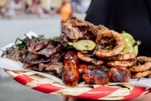 A woven plate lined with paper and topped with a variety of grilled meats freshly grilled at the smoke hall in the Tlacolula Market of Oaxaca. The plate includes chorizo, tasajo, cecina, tripa and chile de agua peppers.