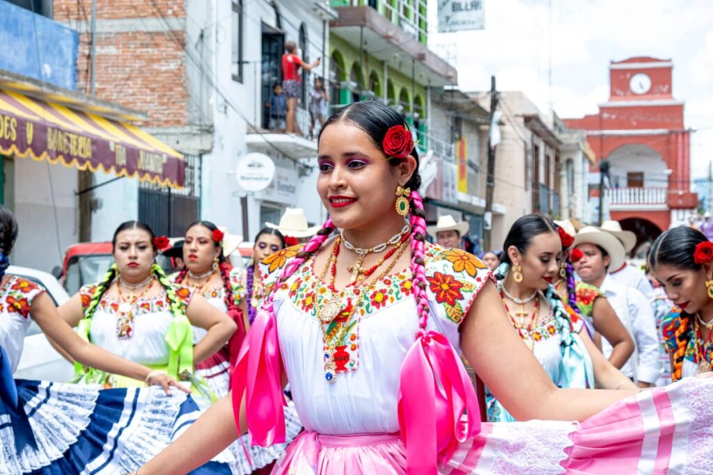 A woman dressed in traditional Oaxacan clothes with pink ribbons braided in her hair lines up for the parade during the Guelaguetza in Oaxaca.