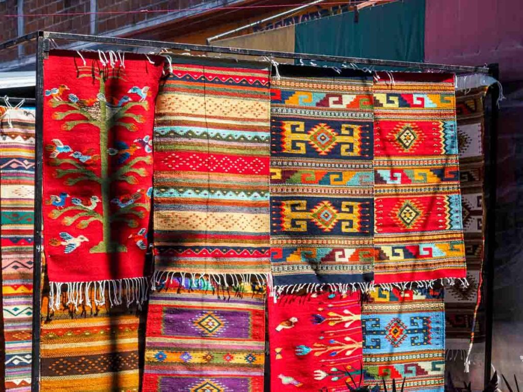 Colorful, hand woven area rugs hang at a market stall at the Tlacolula Sunday Market. They are one of the top things to buy at the markets in Oaxaca.