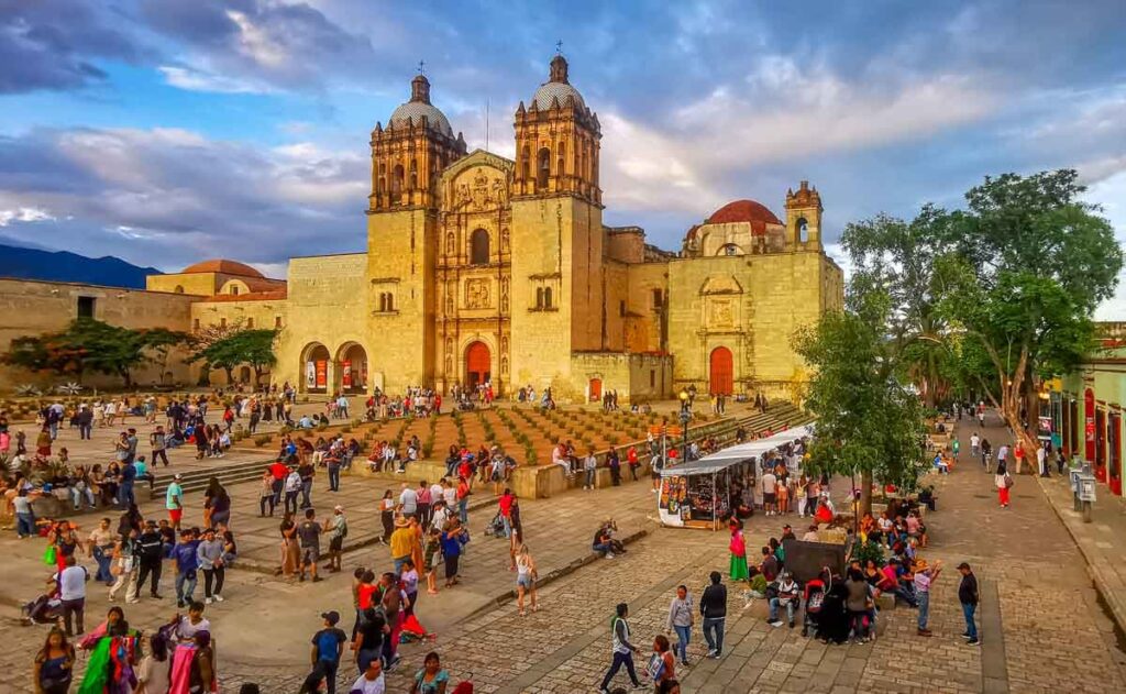 People gather and walk along the street in front of Santo Domingo church in Centro de Oaxaca during the evening hours.