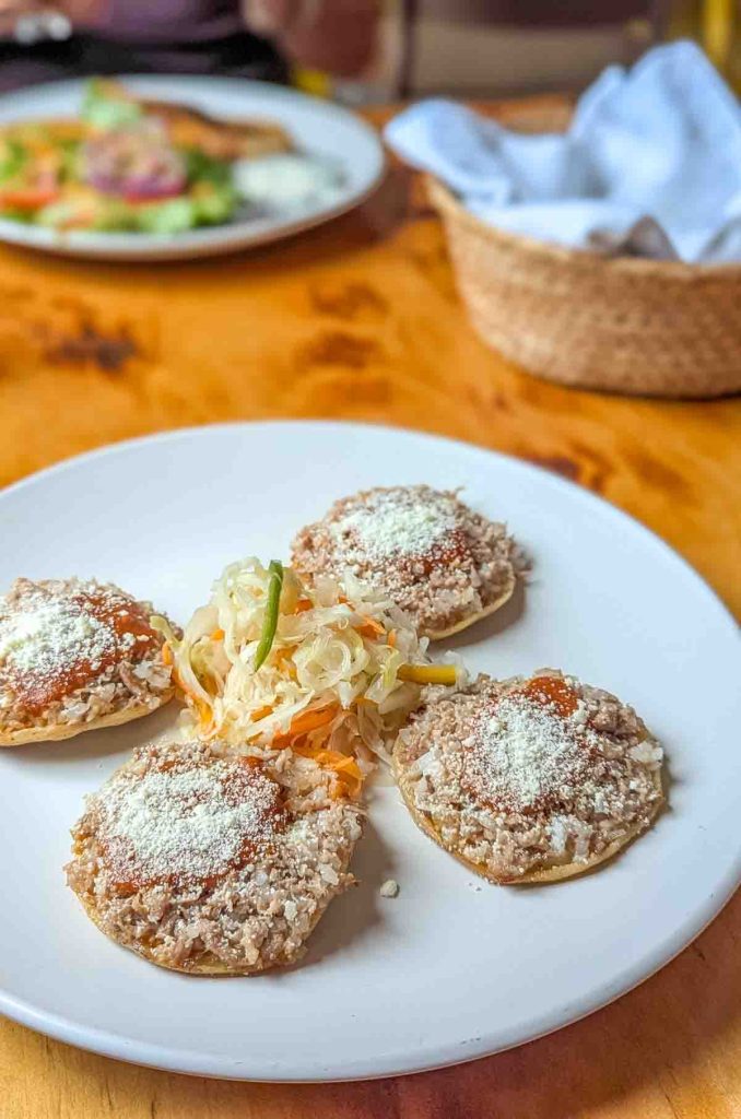 At Totopo Guero, one of the best places to eat in Oaxaca, a white plate with 4 corn discs are topped with minced meat and cheese. In the center is shredded pickled cabbage.