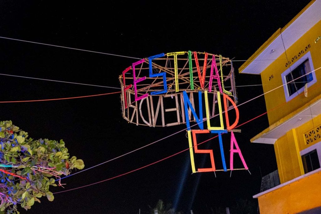 A circular bamboo sign with thin colorful letters that spell out 'Festival Nudista' against the night sky over a street in Zipolite, Oaxaca during the annual nudist festival.