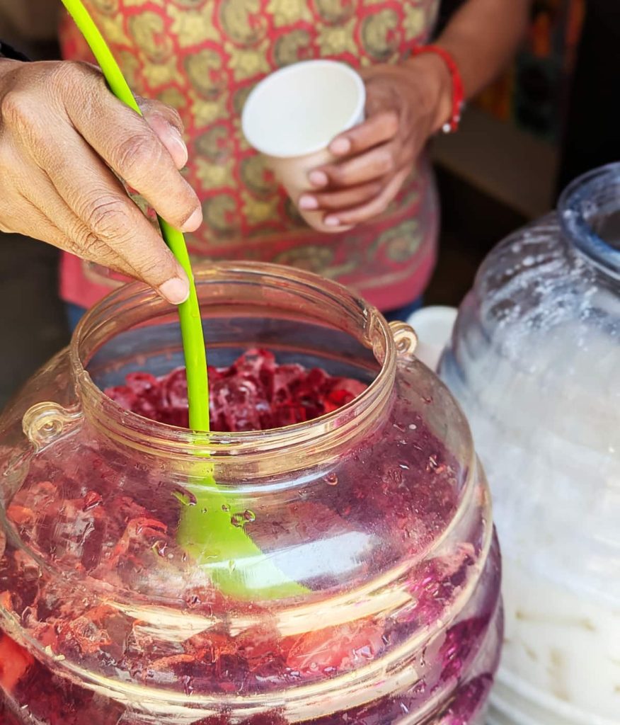 Closeup of a woman's hand using a green plastic ladle to scoop icy jamaica water into a paper cup for the Día Samaritana in Oaxaca City.