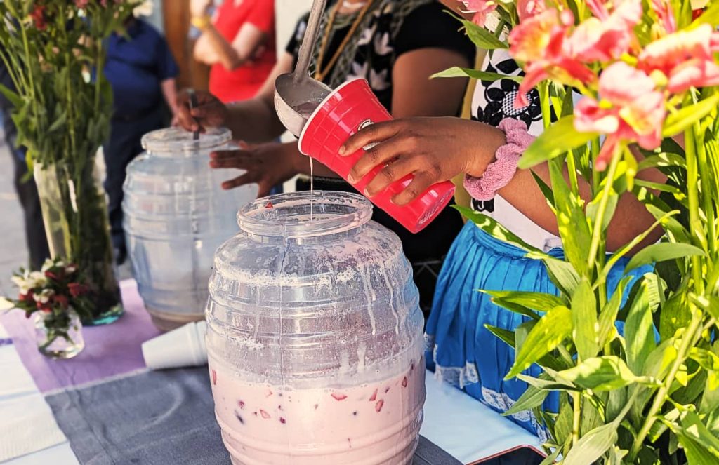 Close up of a woman's hands and she ladles a strawberry and cream drink into a red plastic cup during Día Samaritana in Oaxaca.