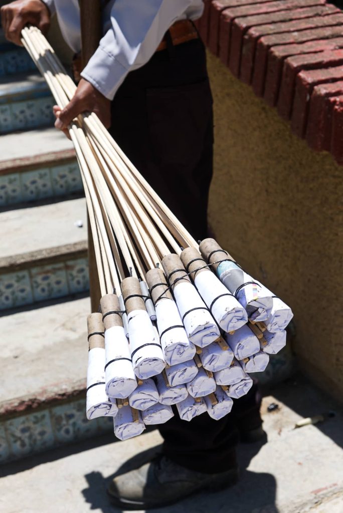 A bundle of cohetes in Oaxaca held by a young man. The cohetes are explosives on the end of a thin wooden stick, covered with white paper and tied with black ribbon.