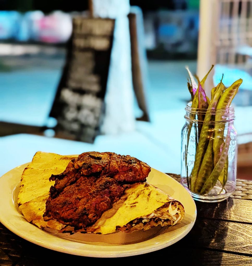 At Gallo Negro restaurant in Puerto Escondido, a white place with a tlayuda topped with grilled ribs. In a jar on the table are guajes, a long, thin green seed pod.